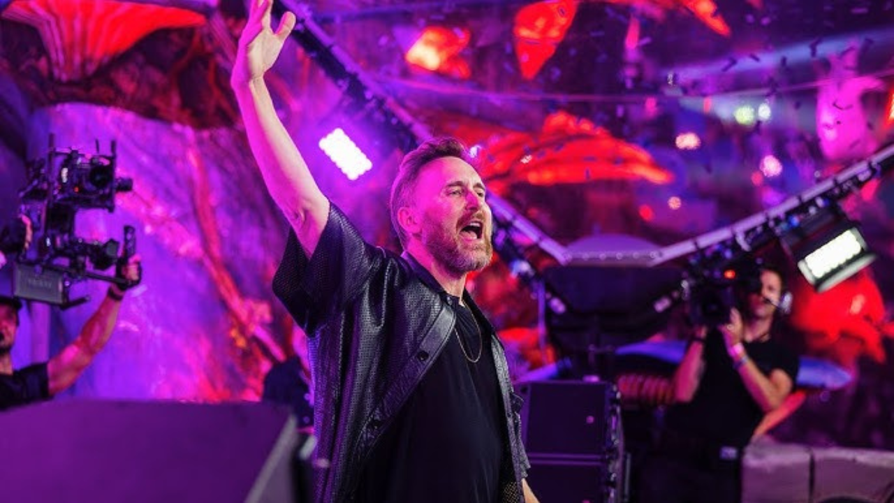 David Guetta, the legendary French DJ and producer, commands the stage at EDC Las Vegas. He's surrounded by a mesmerizing display of vibrant neon lights, lasers, and pyrotechnics that illuminate the massive crowd of fans. Wearing a sleek, modern outfit, David Guetta is seen with a confident smile as he raises his hand to the beat, connecting with the audience in a high-energy moment under the iconic electric sky